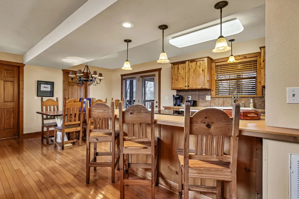 A kitchen view featuring wooden bar stools, a chandelier, rich cabinetry, and double doors leading outside. The scene hints at both the indoor and outdoor dining experience, capturing the transition from kitchen to porch.
