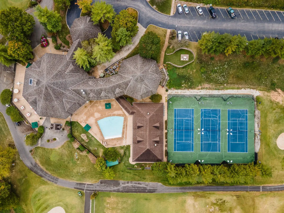 This exterior image showcases a vibrant resort area featuring a swimming pool, tennis courts, clubhouse, and lush surrounding greenery. The scene is lively and appealing, highlighting multiple amenities for group fun and relaxation under sunny skies.