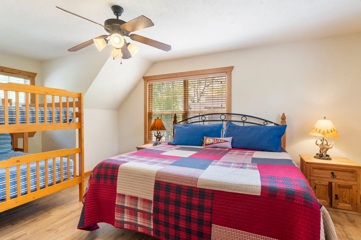 A spacious bedroom featuring a king-size bed with inviting pillows and linens, a twin-over-twin bunk bed on the side, stylish lamps, and warm wooden furnishings. The room exudes comfort and is perfect for family stays, capturing both adult privacy and children's fun.
