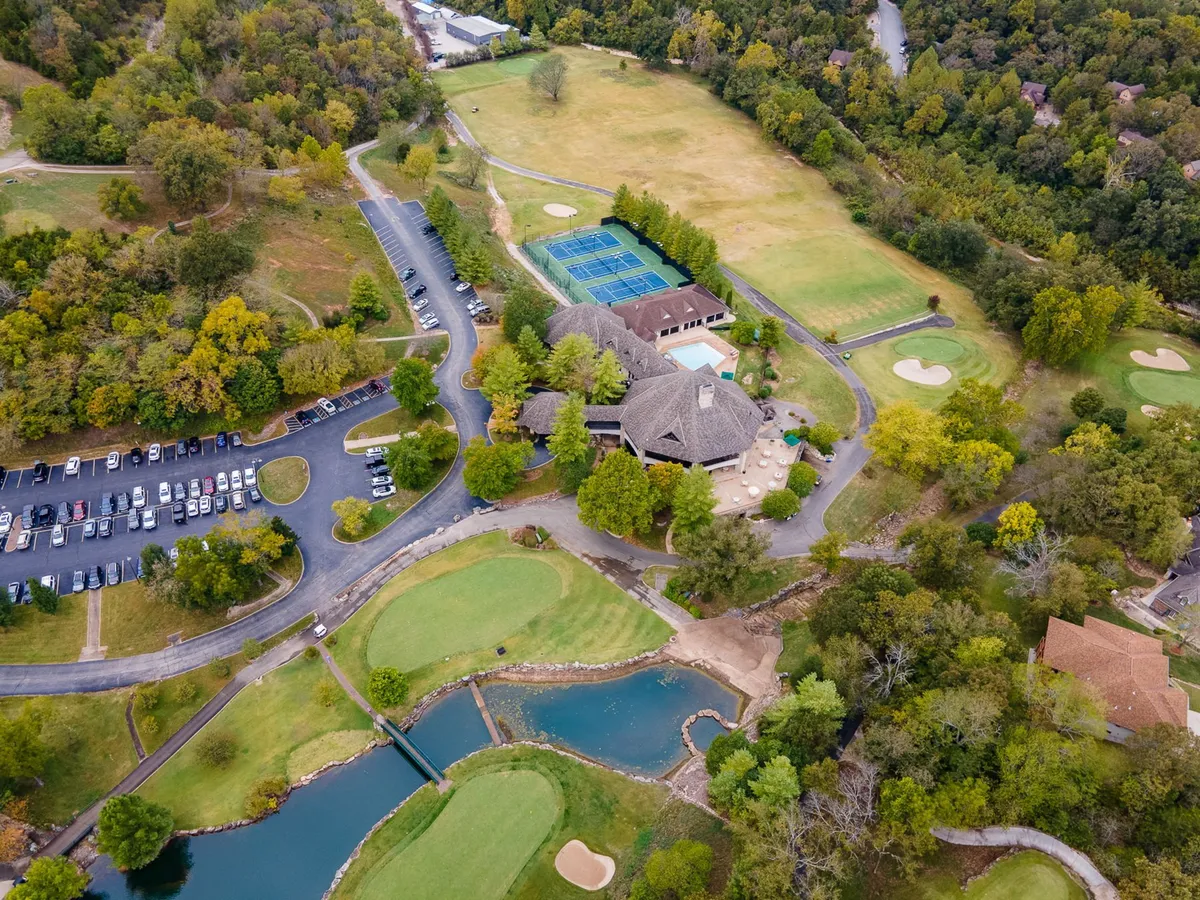 A wide exterior view that captures the golf course alongside the swimming pool, tennis courts, parking area, and the clubhouse. The shot highlights the breadth of resort-style amenities available in the community, with lush landscaping and facilities inviting for a day of recreation and relaxation.