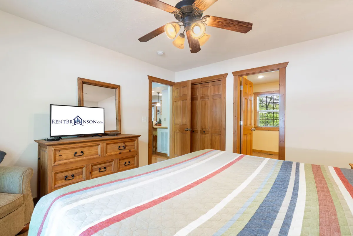 A welcoming bedroom with a striped quilt on the bed, a wooden dresser, and a smart TV displayed prominently. The space feels homey and equipped for relaxation, with entertainment at your fingertips.
