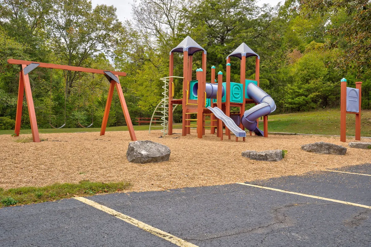 A bright, joyful exterior image of a playground with swings and climbing structures surrounded by greenery. The scene is inviting for families, signaling fun and safe spaces for children to play and explore.