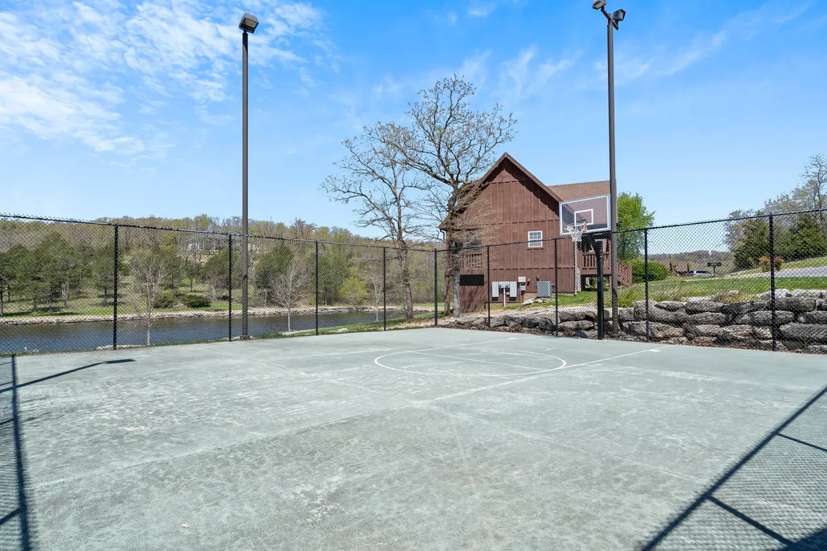 This lively exterior scene focuses on a basketball court framed by trees, with views of a peaceful lake and a nearby building. The area is ready for games, picnics, or community gatherings, blending energetic activity with serene resort scenery.